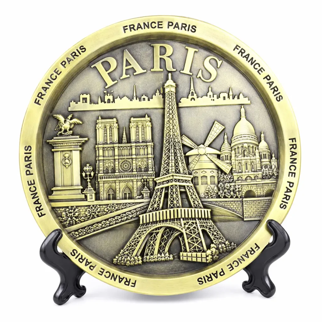 Brass-tone Paris souvenir plate with Eiffel Tower and landmark relief on a black stand against a white background