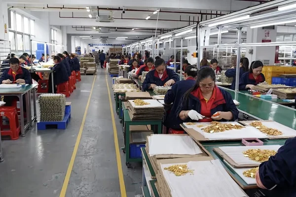 Custom souvenir manufacturing factory showing workers assembling and processing personalized souvenir products on a large-scale production line.